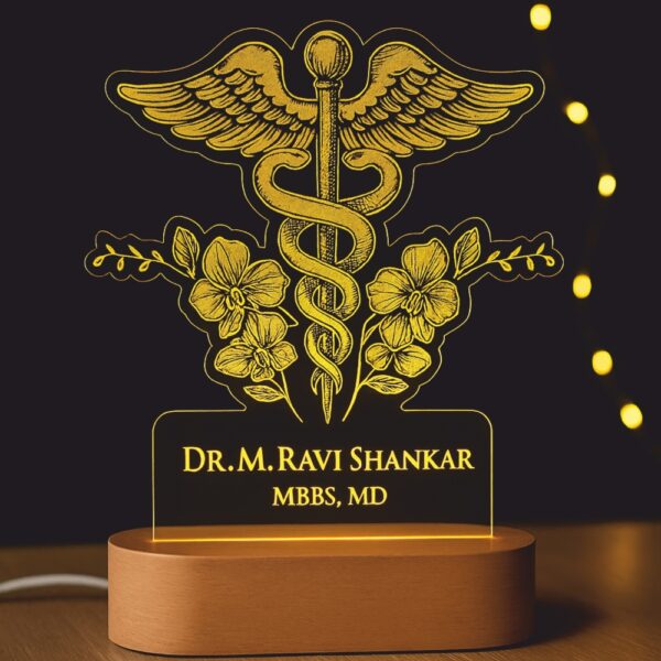 Custom LED night lamp with an engraved Caduceus medical symbol and floral accents, glowing warmly with the name “Dr. M. Ravi Shankar – MBBS, MD” on a wooden base, placed outdoors at dusk.