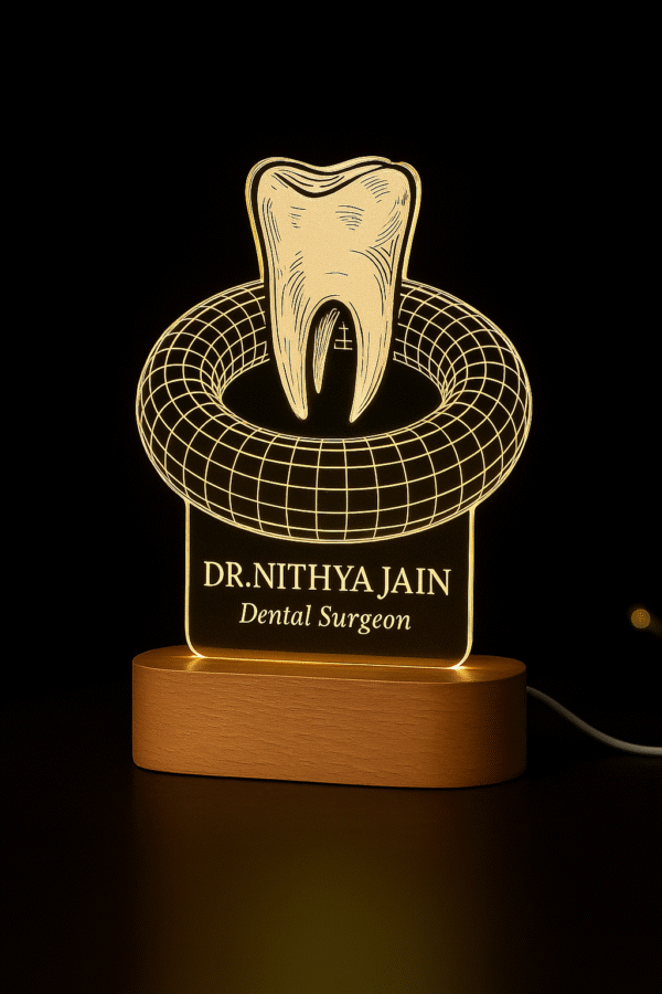 A custom LED night lamp featuring a 3D tooth design with the name “Dr. Nithya Jain, Dental Surgeon” engraved on illuminated acrylic with a wooden base.
