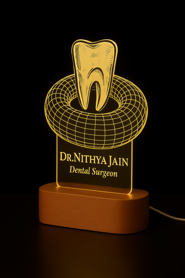 A custom LED night lamp featuring a 3D tooth design with the name “Dr. Nithya Jain, Dental Surgeon” engraved on illuminated acrylic with a wooden base.