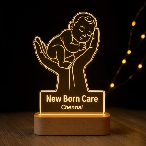 Custom LED night lamp featuring an engraved outline of a baby cradled in two hands, with the text “New Born Care – Chennai,” glowing warmly on a wooden base in a neonatal setting.