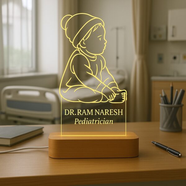 LED night lamp featuring an engraved outline of a baby sitting with a beanie, with the name “Dr. Ram Naresh – Pediatrician” glowing warmly on a wooden base in a hospital setting.