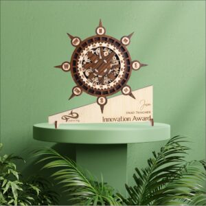 Wooden compass-themed award with intricate gear detailing, engraved base text, and nautical wheel design placed on a green pedestal.