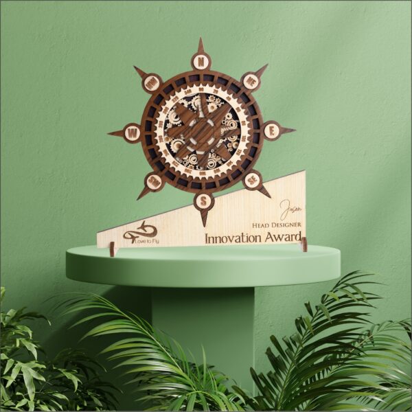 Wooden compass-themed award with intricate gear detailing, engraved base text, and nautical wheel design placed on a green pedestal.