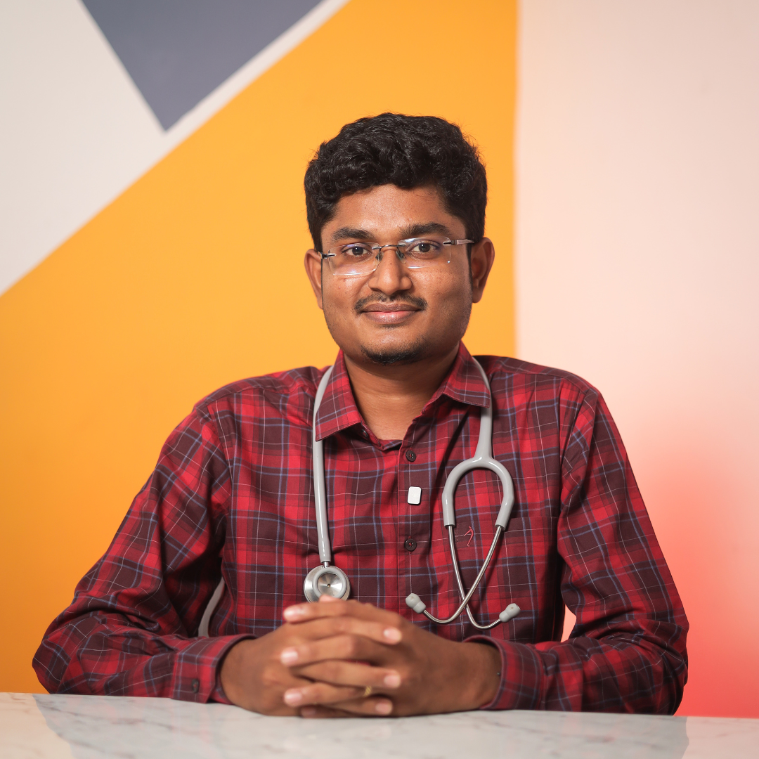 Dr. Hariharasudhan, Dermatologist, wearing a red checked shirt with stethoscope, seated at desk.